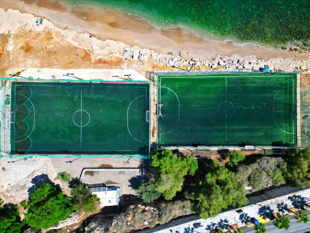 Top-down aerial image (90°) of two football fields by the sea in Votsalakia, Piraeus, showcasing aerial photography services by Perigon Perspective for businesses, municipalities, construction, tourism, and maritime enterprises.